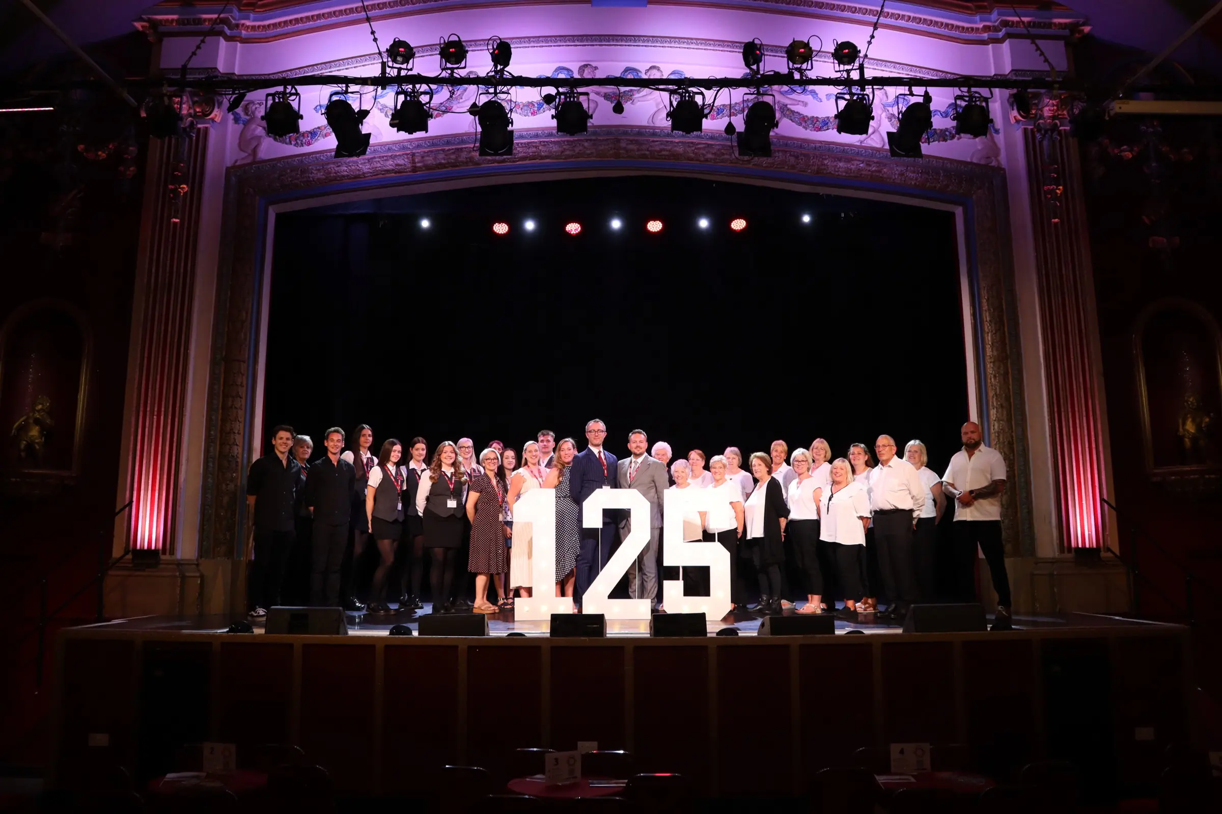 Pavilion staff and volunteers gathered on stage behind illuminated 125 numbers