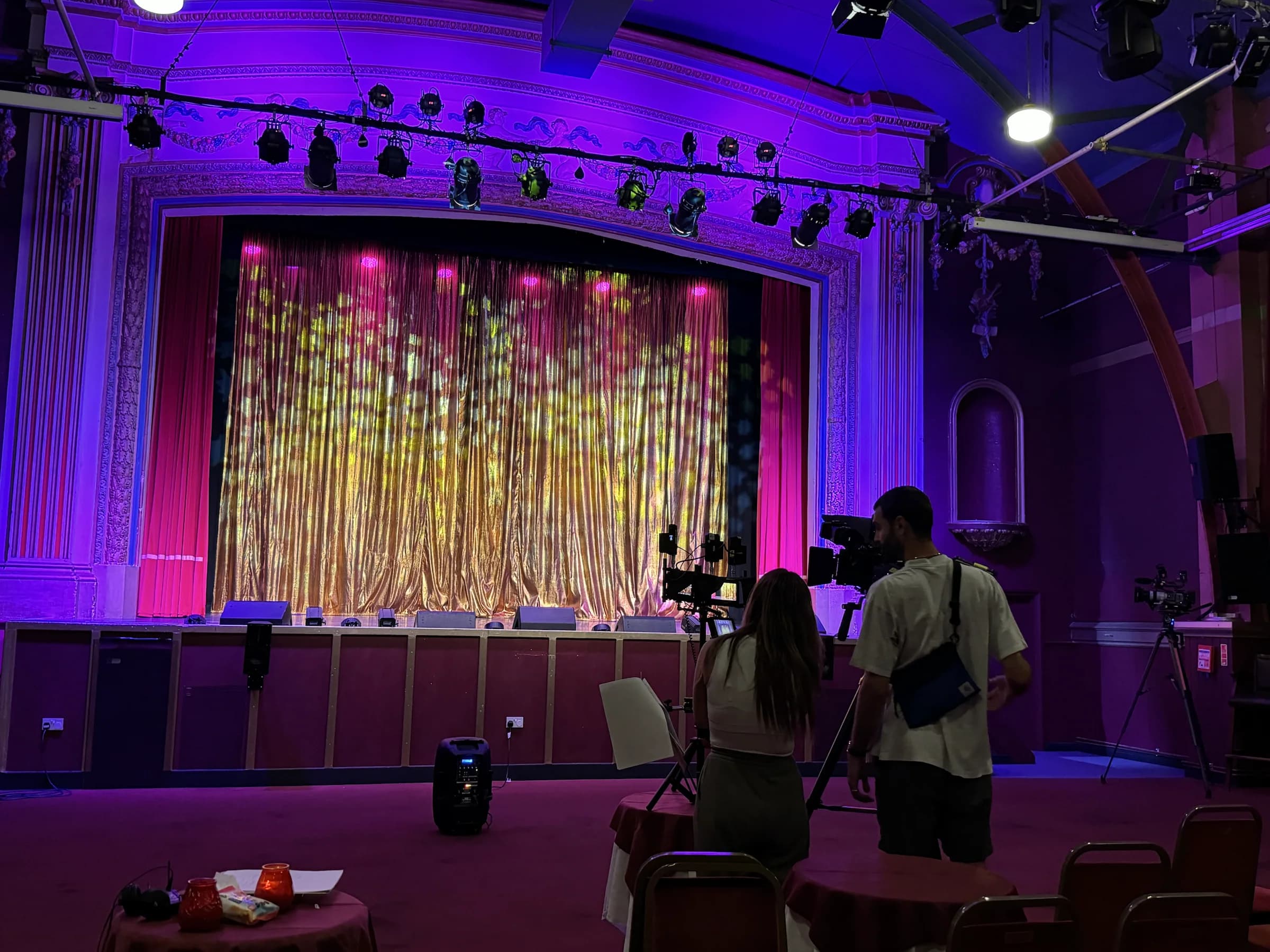 Two production team members standing beside camera equipment in the auditorium